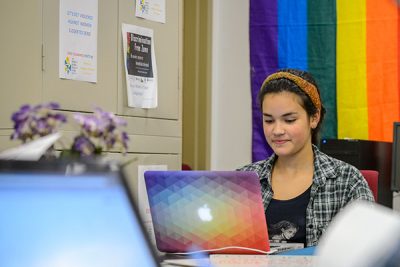 A student uses a laptop computer in front of the rainbow flag..