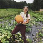 Nicole Davidow standing in a vegetable field holding a pumpkin